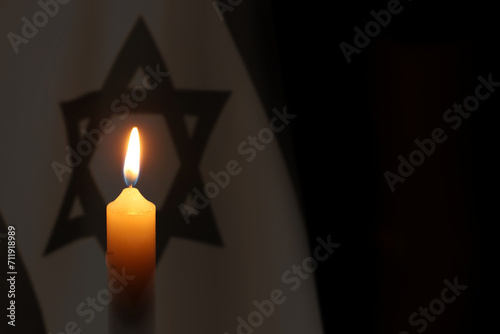 Burning candle against flag of Israel on black background photo