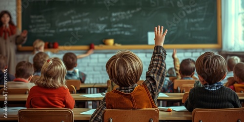 A child in a school class raises his hand to ask the teacher. Scene seen from behind