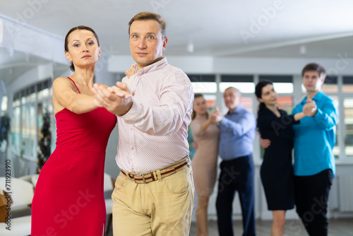 Positive adult couple enjoying slow foxtrot in dance studio. Amateur social dancing concept..