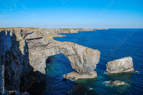 Natural rock arch known as The Green Bridge of Wales on the coast of Pembrokeshire, UK. Blue water and cliff landscape