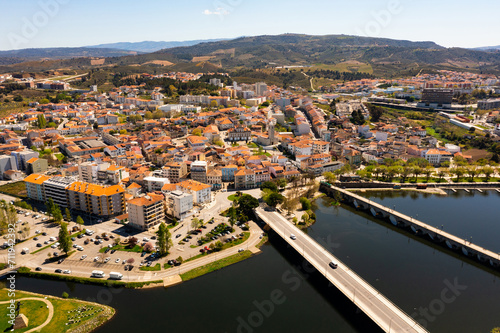 Picturesque aerial view of residential districts of Mirandela city with brownish tiled roofs and two bridges crossing Tua river on spring day, Braganca, Portugal
