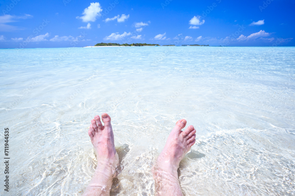 Man's feet in the water, relaxation on a tropical island in the Maldives Man's feet in the water, relaxation on a tropical island in the Maldives