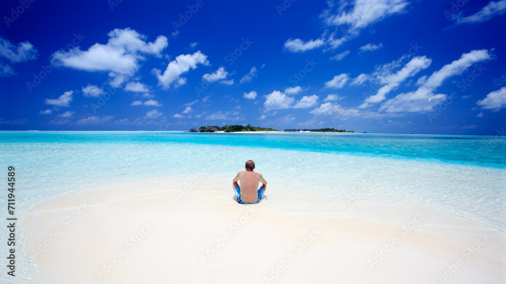 Man sitting on the sand on a tropical island in the Maldives Man sitting on the sand on a tropical island in the Maldives