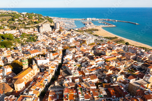 Scenic drone view of coastal small Catalan town of Arenys de Mar overlooking reddish roofs of residential buildings and parish church of Santa Maria on sunny day, Barcelona, Spain ..