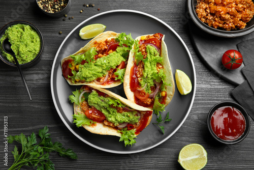 Delicious tacos with guacamole, meat and vegetables on wooden table, flat lay