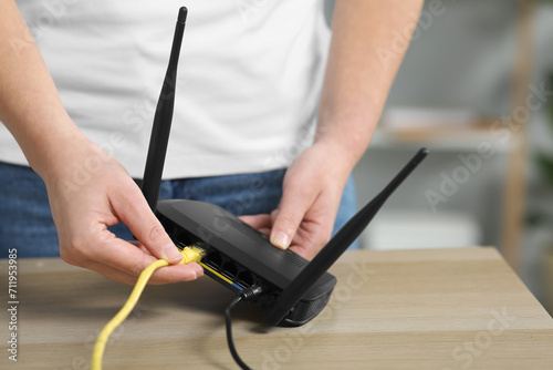 Woman inserting ethernet cable into Wi-Fi router at table indoors, closeup