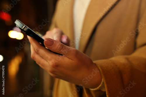 Woman using smartphone on blurred background, closeup