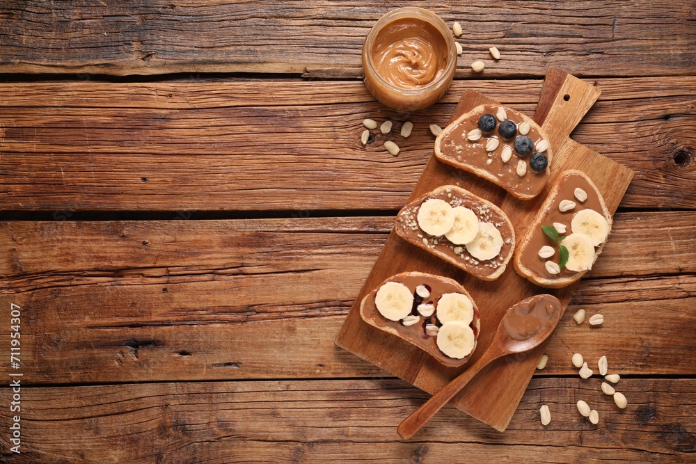 Toasts with tasty nut butter, banana slices, blueberries and peanuts on wooden table, flat lay. Space for text Toasts with tasty nut butter, banana slices, blueberries and peanuts on wooden table, flat lay. Space for text