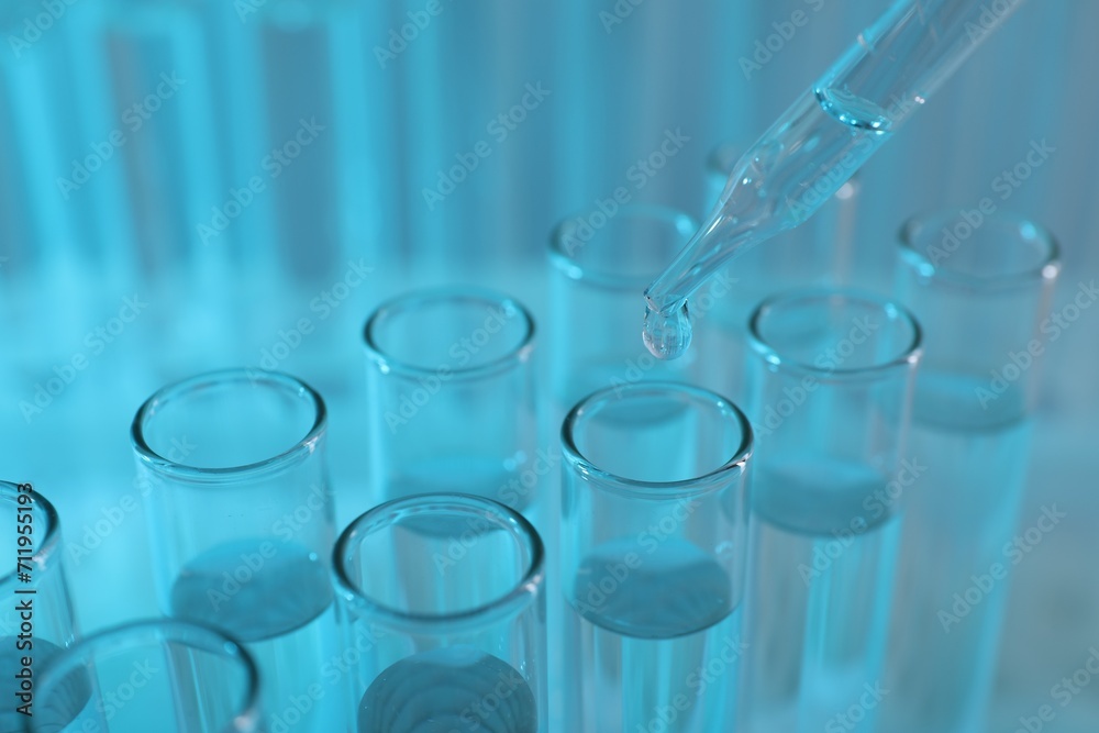 Laboratory analysis. Dripping liquid from pipette into glass test tube on light blue background, closeup Laboratory analysis. Dripping liquid from pipette into glass test tube on light blue background, closeup