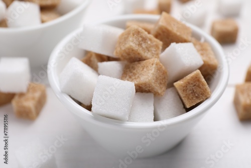 Different sugar cubes in bowl on white table, closeup