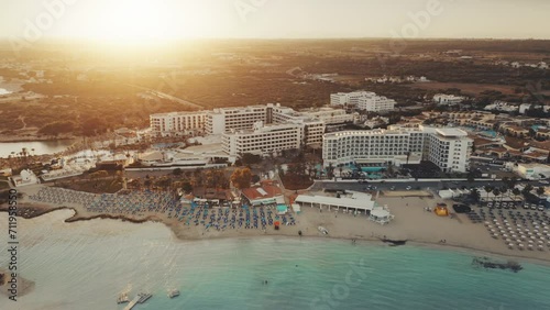 Aerial view of Mediterranean coastline in the sunset. Turquoise crystal water on Nissi Beach, Ayia Napa, Cyprus. Hotels resort complex on the first line. Travel destination landscape. Summer vacation. photo