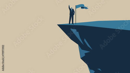A man is raising his hand on a cliff. There is flag around.