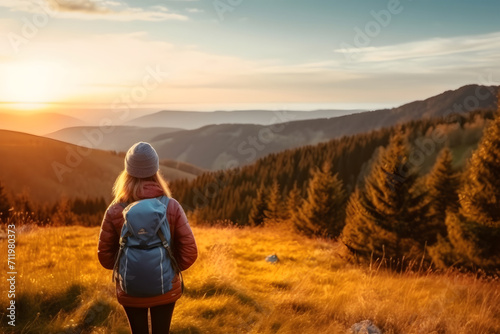 lone traveler stands amidst tall grass, facing rolling hills and majestic mountains. The warm light of either sunrise or sunset bathes the landscape in golden hues