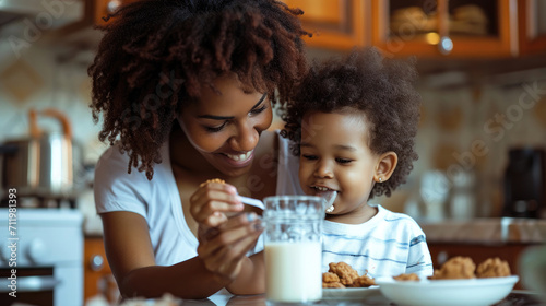 Happy African American family: Mother and little son eat cookies with milk for breakfast at home