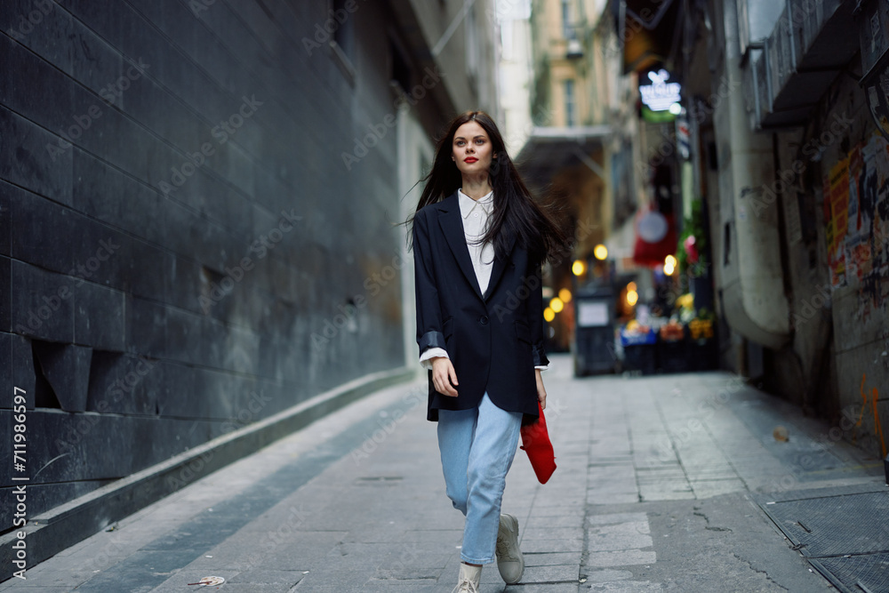Fashion woman tourist in stylish clothes in a jacket and red beret walking down a narrow city street flying hair and happy travel, French style, cinematic color, retro style.