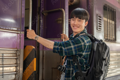 A happy Asian man backpacker is getting on the train, travel somewhere on his summer vacation.
