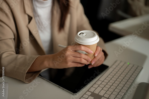 Close-up image of a businesswoman holding a coffee cup, sipping coffee at her office desk.