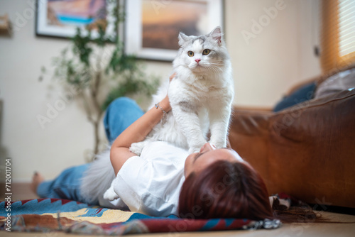 Young woman playing with cat on carpet at home.