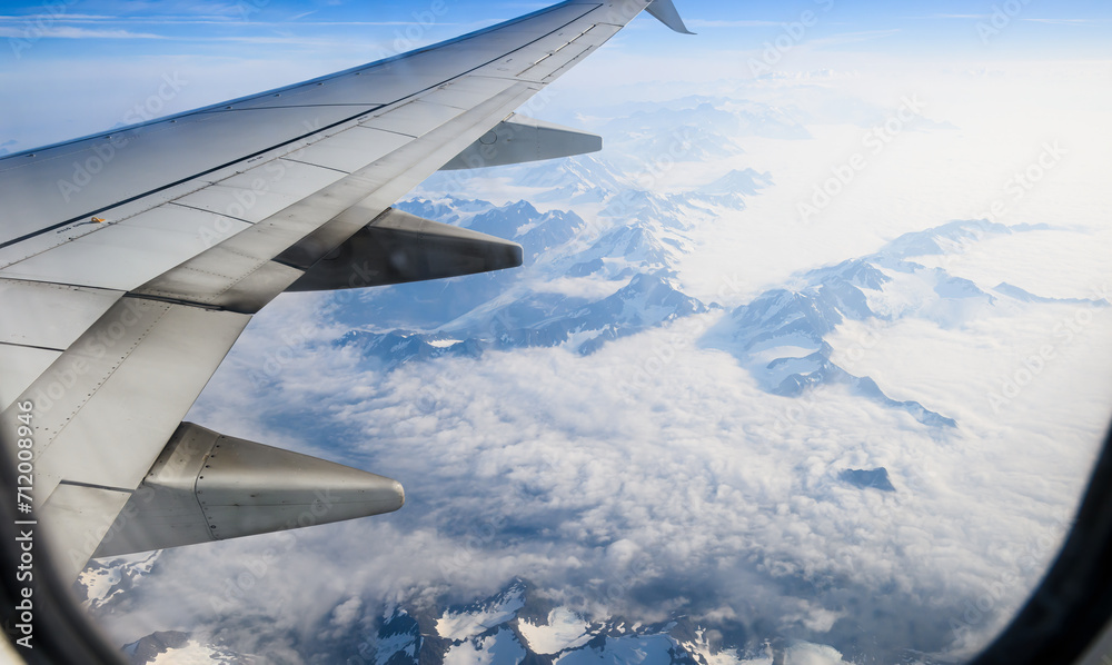 Aerial view of high mountain peaks above clouds. Airplane flying towards Anchorage. Alaska. USA.
