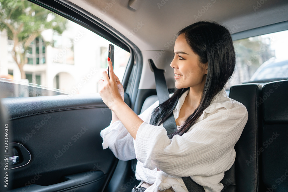 Asian Woman Traveler sitting in car back seats using smartphone take a photo while travel by taxi service put on safety belt. Passenger in car traveling to destination on a bright day