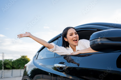 Young beautiful asian business women getting new car. Happy smiling female driving vehicle on the road Sticking her head outta the windshield with sun light. Business woman buying driving new car © Chanakon