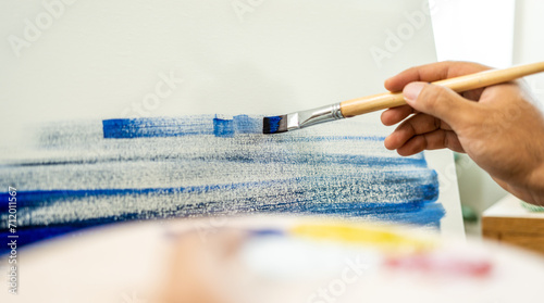 Asian man artist working on painting with brush and variant acrylic color. Man artist painter on canvas in creative studio as art concept