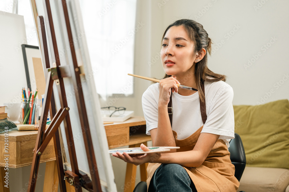 Asian woman artist working on painting with brush and variant acrylic color. Female artist painter on canvas in creative studio as art concept Asian woman artist working on painting with brush and variant acrylic color. Female artist painter on canvas in creative studio as art concept