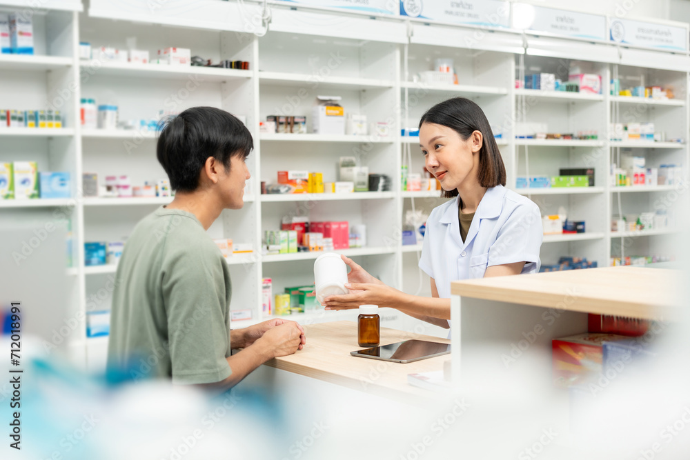 Fototapeta premium Pharmacist recommends medicines to customers.Taking the questions of medication. Asian female pharmacist giving prescription medications to customers at drugstore shelves.