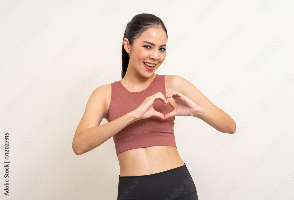 Young beautiful smiling asian woman with sportswear showing mini heart on isolated white background. Portrait happy healthy slim fit and firm latin attractive sporty woman heart sign pose