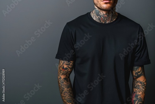 Man with tattoos wearing a black t shirt standing against a grey background. photo