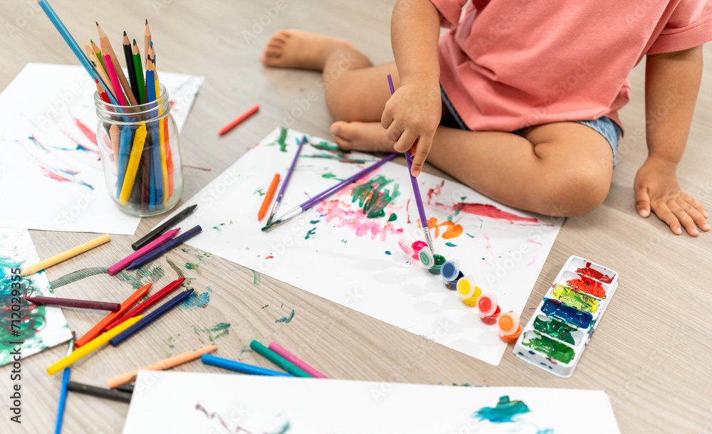 Happy moment little cute girl creating and water color painting activity with paint brushes on frame canvas at living room. Kids activity. Child physical, Emotional, Cognitive development concept. Happy moment little cute girl creating and water color painting activity with paint brushes on frame canvas at living room. Kids activity. Child physical, Emotional, Cognitive development concept.