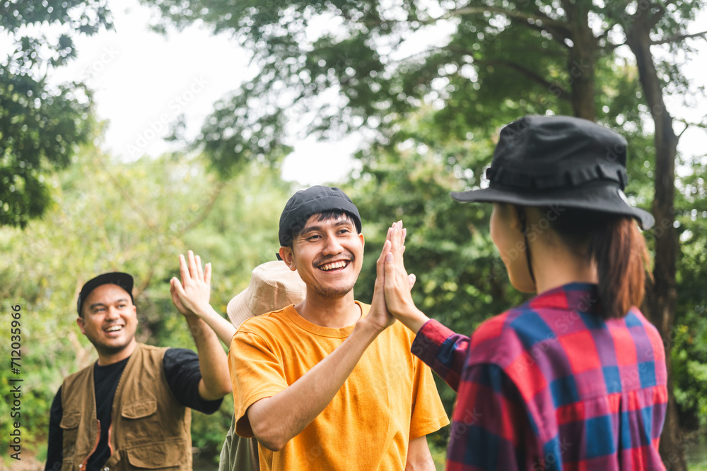 Group of young traveller people giving high five for friendship while camping in nature trip. Happy asian people group friend travel together. Enjoying camping on weekend vacation time.