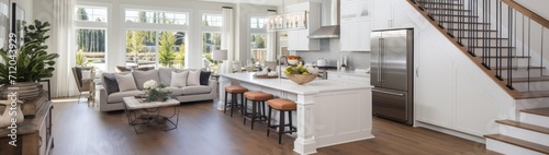 Kitchen and living room interior in new luxury home with open concept floor plan. Features large island with farmhouse sink, hardwood floors, and stairs to second story.