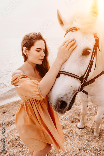 A white horse and a woman in a dress stand on a beach, with the