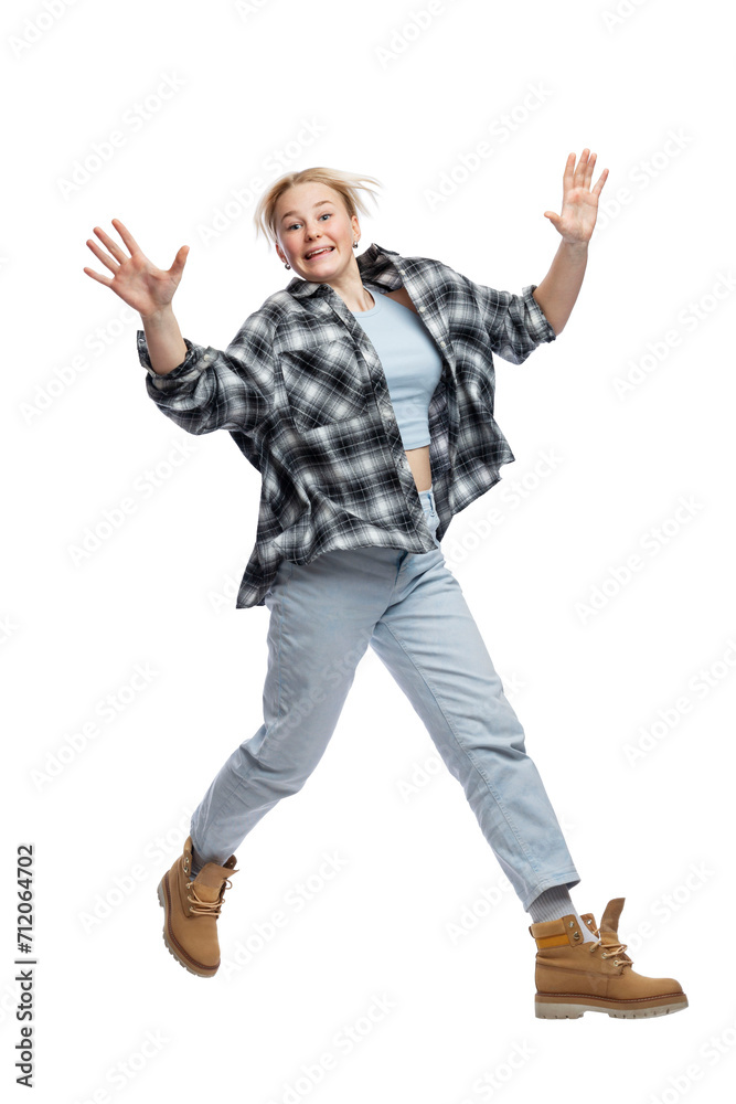 A young girl jumps funny. Cute laughing blonde girl in jeans, blue top and plaid shirt. Activity, energy and positivity. Isolated on a white background. Vertical. Full height. A young girl jumps funny. Cute laughing blonde girl in jeans, blue top and plaid shirt. Activity, energy and positivity. Isolated on a white background. Vertical. Full height.