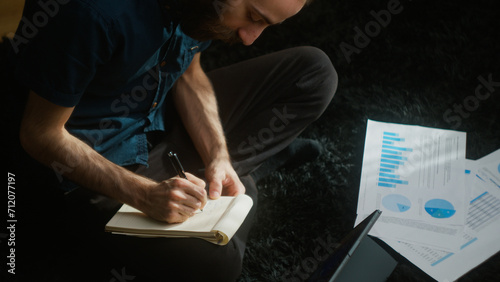 High agle shot of young adult student with long hair sitting on the carpet on the floor using tablet computer writing notes 	
 photo