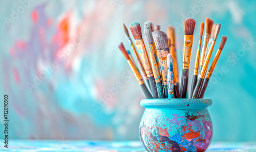 Art brushes in paint in a creative pot on a blue background with space for copy and text.