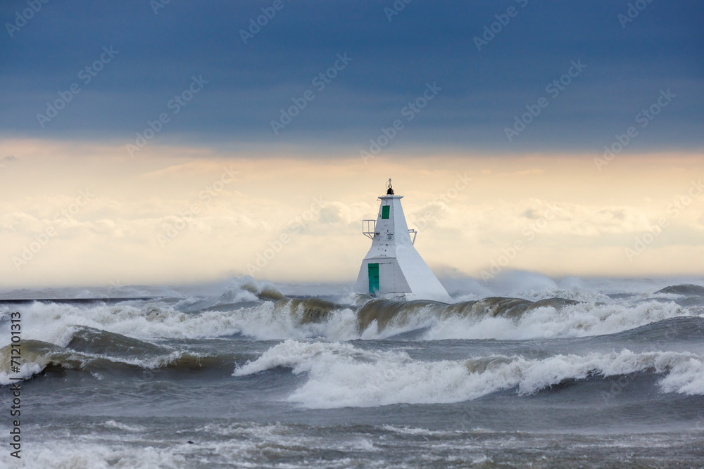 the sea waves crash in front of the light house as the sun sets