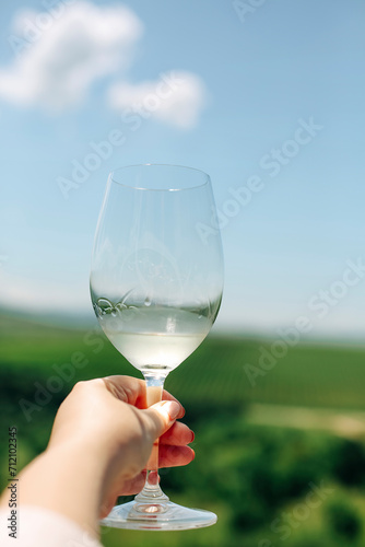 Twisting glass of white wine, vineyard in the background