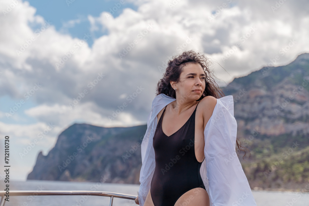 Woman on a yacht. Happy model in a swimsuit posing on a yacht against a blue sky with clouds and mountains