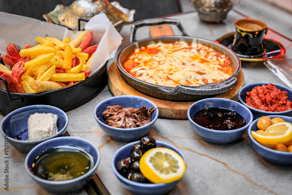Traditional Turkish breakfast kahvalti with eggs in a skillet, jams, olives, cheese, dips, fries and Turkish coffee at a restaurant, Istanbul, Turkey