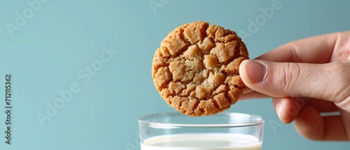 Close-Up of a Hand Holding a Cookie, Glass of Milk. Set Against a Vibrant Blue Background, Bright Lighting Enhances the Anticipation of the Dunking Moment.
