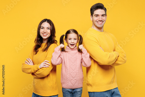 Young parents mom dad with child kid girl 7-8 years old wearing pink knitted sweater casual clothes hold hands crossed folded do winner gesture isolated on plain yellow background. Family day concept. photo