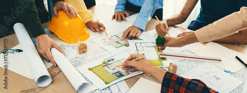 Fototapeta samoprzylepna Professional architect cooperate with engineer discussing the use of green design in eco house project on table with blueprint and architectural equipment scatter around. Closeup. Delineation.
