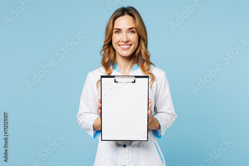Female happy smiling doctor woman wears white gown suit work in hospital clinic office hold clipboard with blank area medical documents isolated on plain blue background. Health care medicine concept. photo