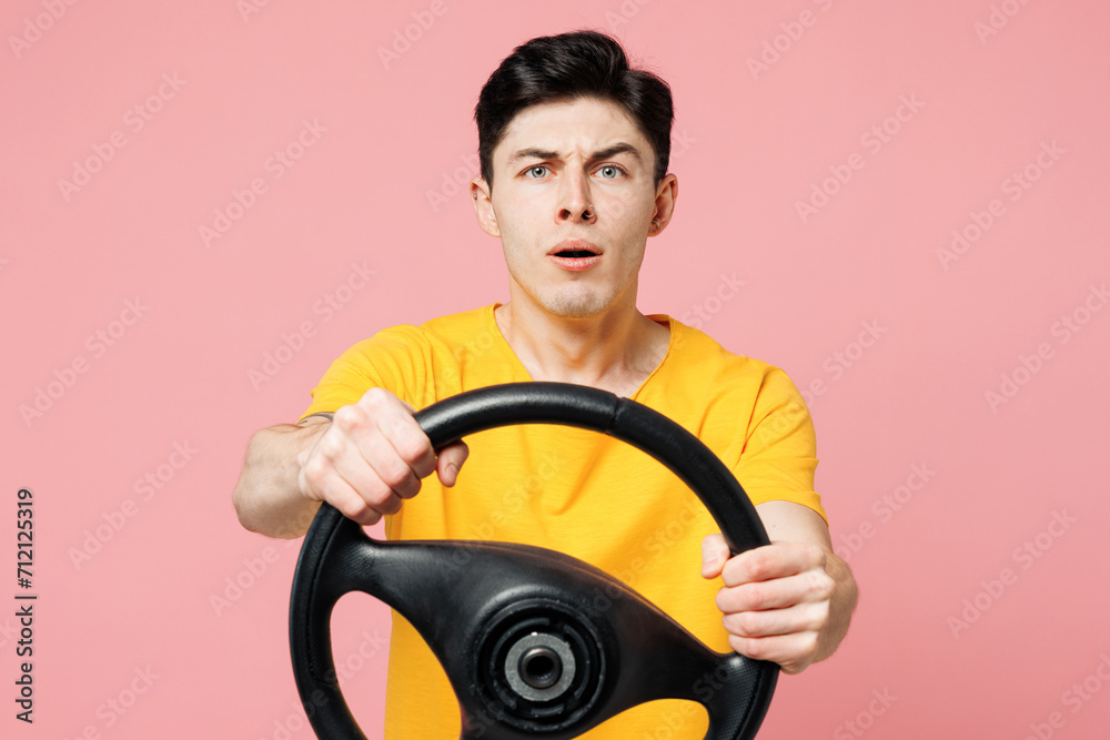 Young shocked astonished Caucasian man wear yellow t-shirt casual clothes hold steering wheel driving car look camera isolated on plain pastel light pink background studio portrait. Lifestyle concept Young shocked astonished Caucasian man wear yellow t-shirt casual clothes hold steering wheel driving car look camera isolated on plain pastel light pink background studio portrait. Lifestyle concept