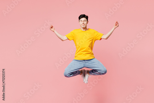Full body young man wears yellow t-shirt casual clothes jump high hold spread hands in yoga om aum gesture relax meditate try to calm down isolated on plain pastel pink background. Lifestyle concept.