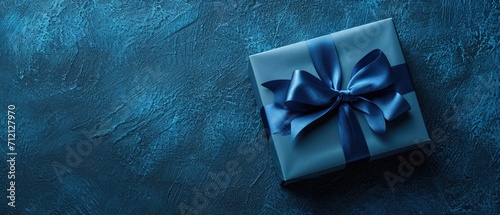 A small, luxurious gift box with a blue bow, positioned on a dark blue table. Side view in monochrome, Ai Generated. © Crazy Juke