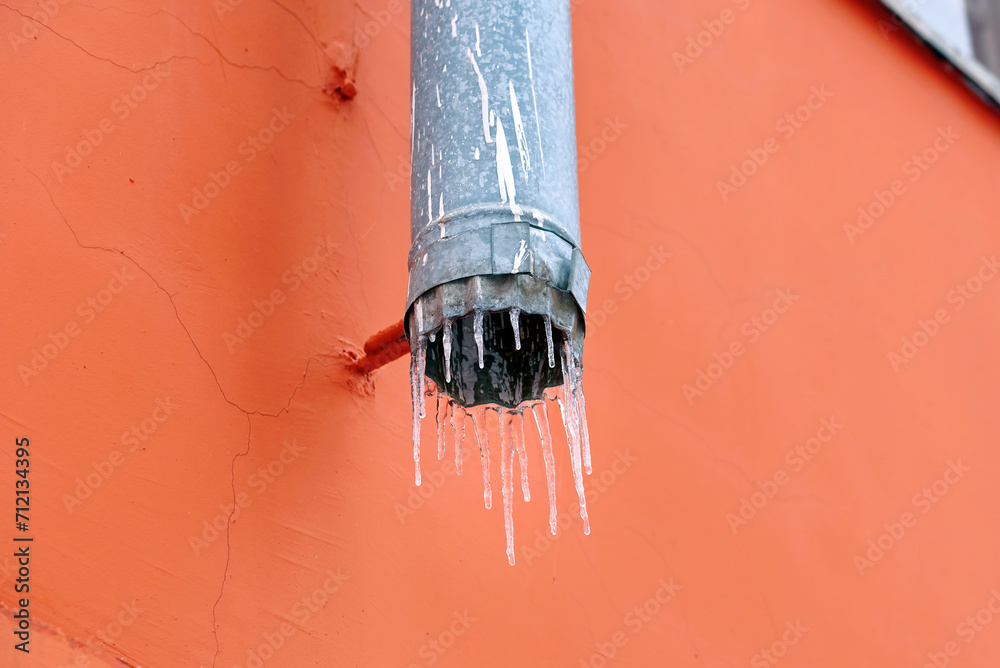 Downspout with icicles on red wall background. Icicles hanging from
