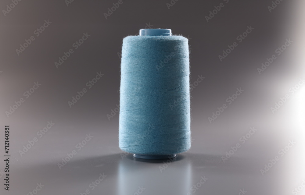 Close-up of blue colour thread spool on grey background, thread for dressmaking industry, yarn for sewing. Hobby, tailoring, atelier concept. Copy space Close-up of blue colour thread spool on grey background, thread for dressmaking industry, yarn for sewing. Hobby, tailoring, atelier concept. Copy space